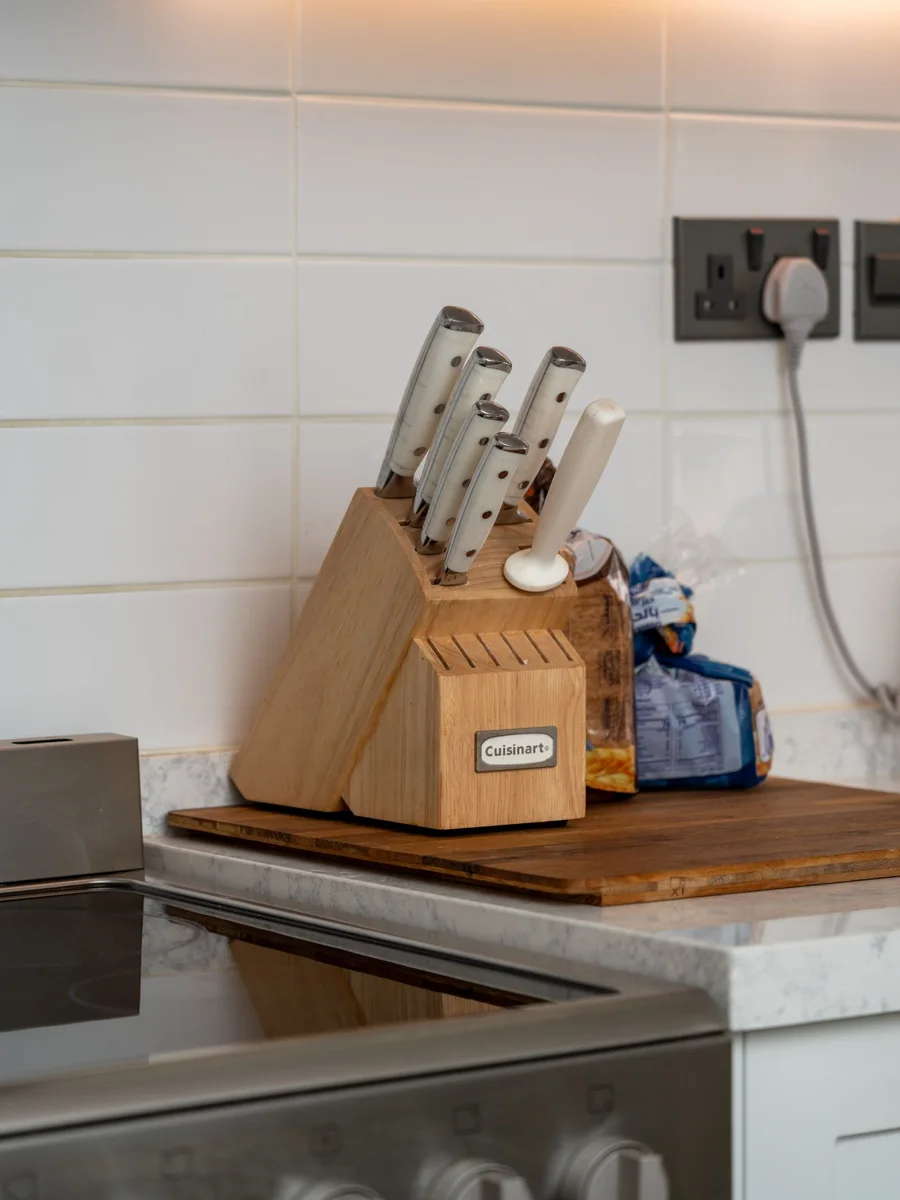 Wooden knife block on a kitchen counter with four knives in slanted slots and a sharpening steel beside it
