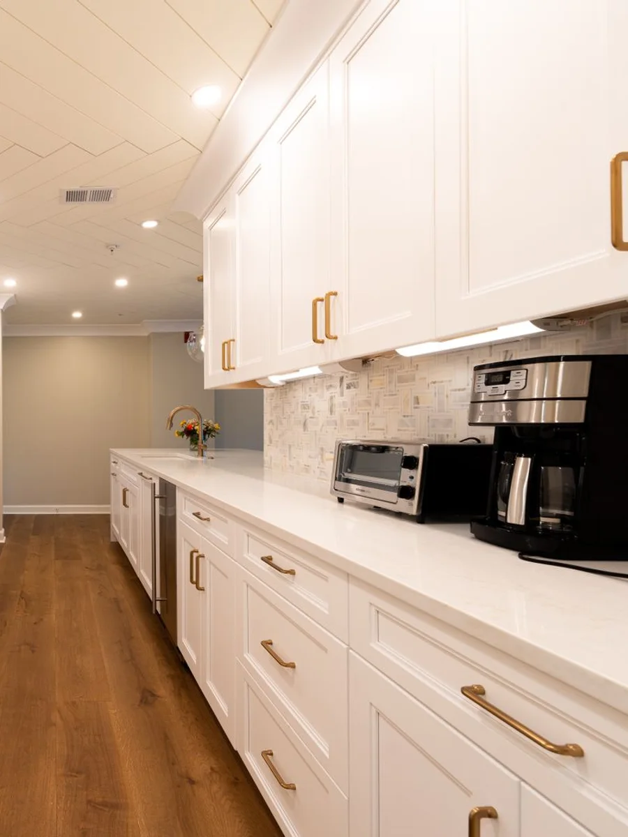 Renovated galley kitchen with painted oak cabinets, laminate counters, white tile backsplash, and new under-cabinet lighting