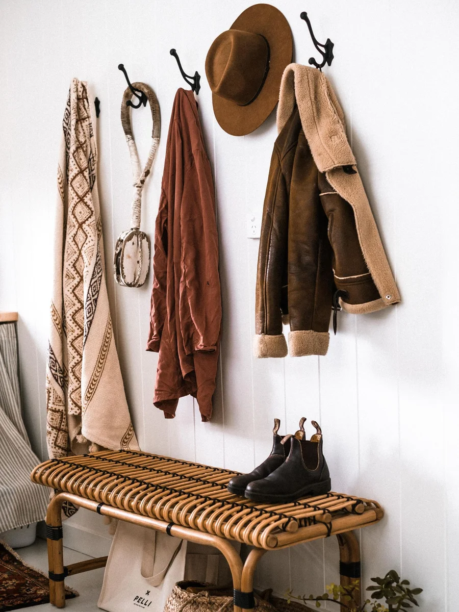 Wooden mudroom bench with open cubbies below, coats on hooks above, and a pair of wet boots on a tray