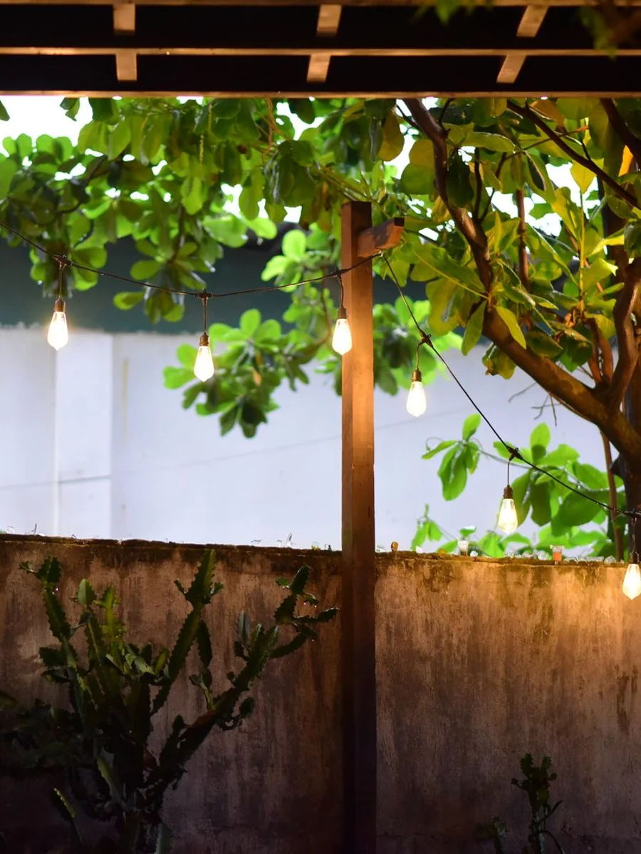 Covered patio at dusk with string lights overhead, small lanterns along a low wall, and a lit table between two chairs