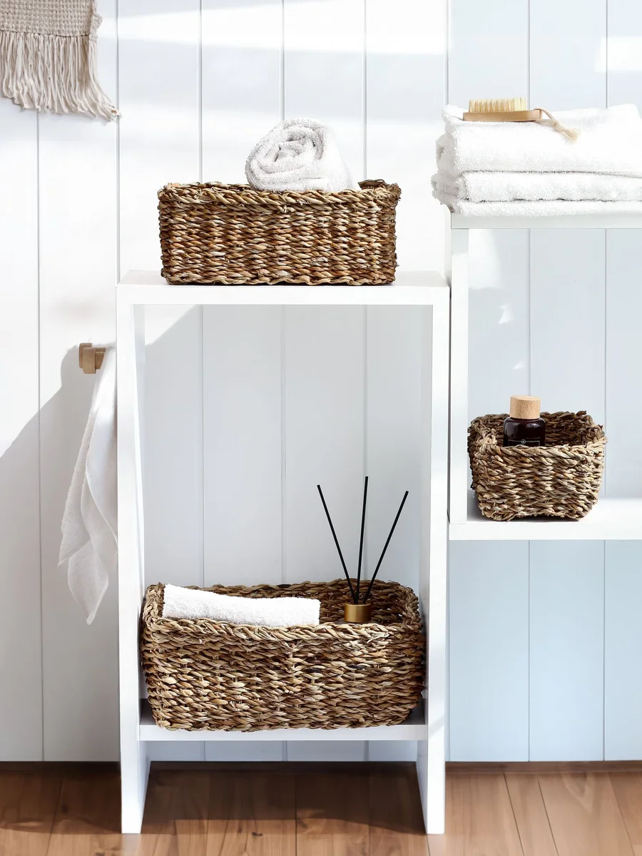 Narrow bathroom with a slim over-the-toilet cabinet, clear stacked bins under the sink, and folded towels in a woven basket
