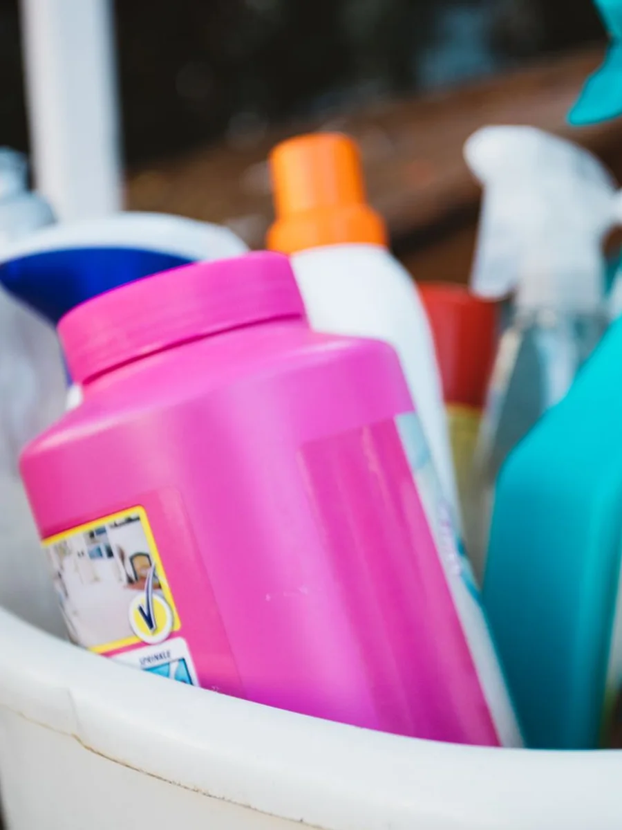 Kitchen counter at night with a cleaning caddy, folded cloths, and a spray bottle under warm overhead light